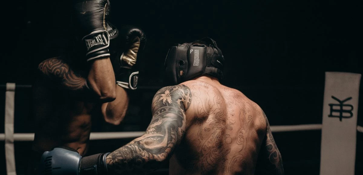 Dos boxeadores, uno defendiendo su rostro y el otro de espaldas con los brazos abiertos.