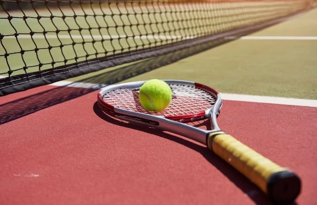 Pelota de tenis sobre una raqueta con una red al fondo en una cancha de tenis.